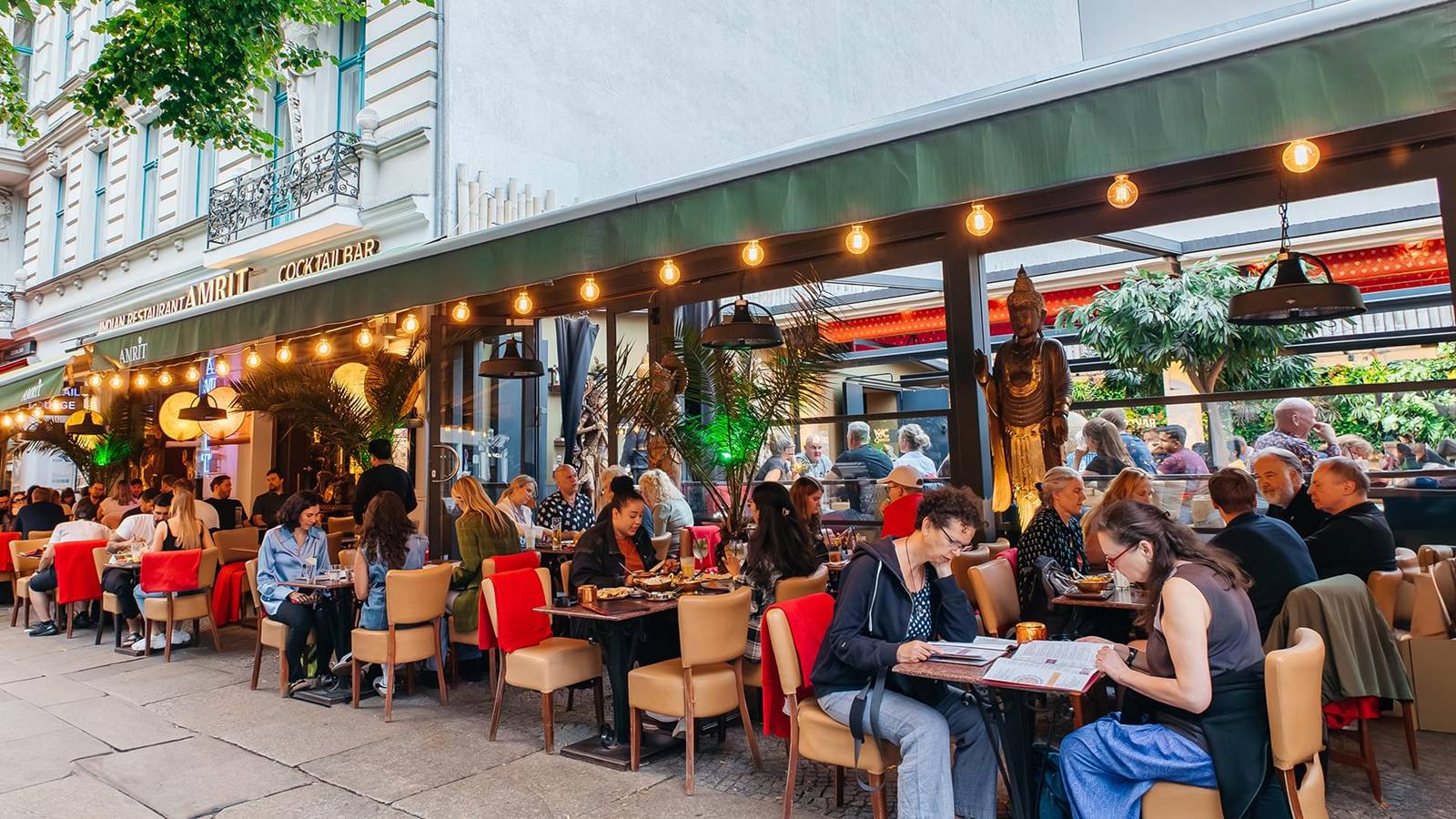 Het terras van AMRIT aan de Oranienburger Straße, vol gasten onder een luifel met lampjes