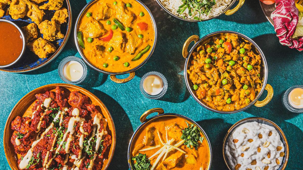 Bovenaanzicht van verschillende curry's, rijst en raita in koperen pannetjes op een blauwe tafel