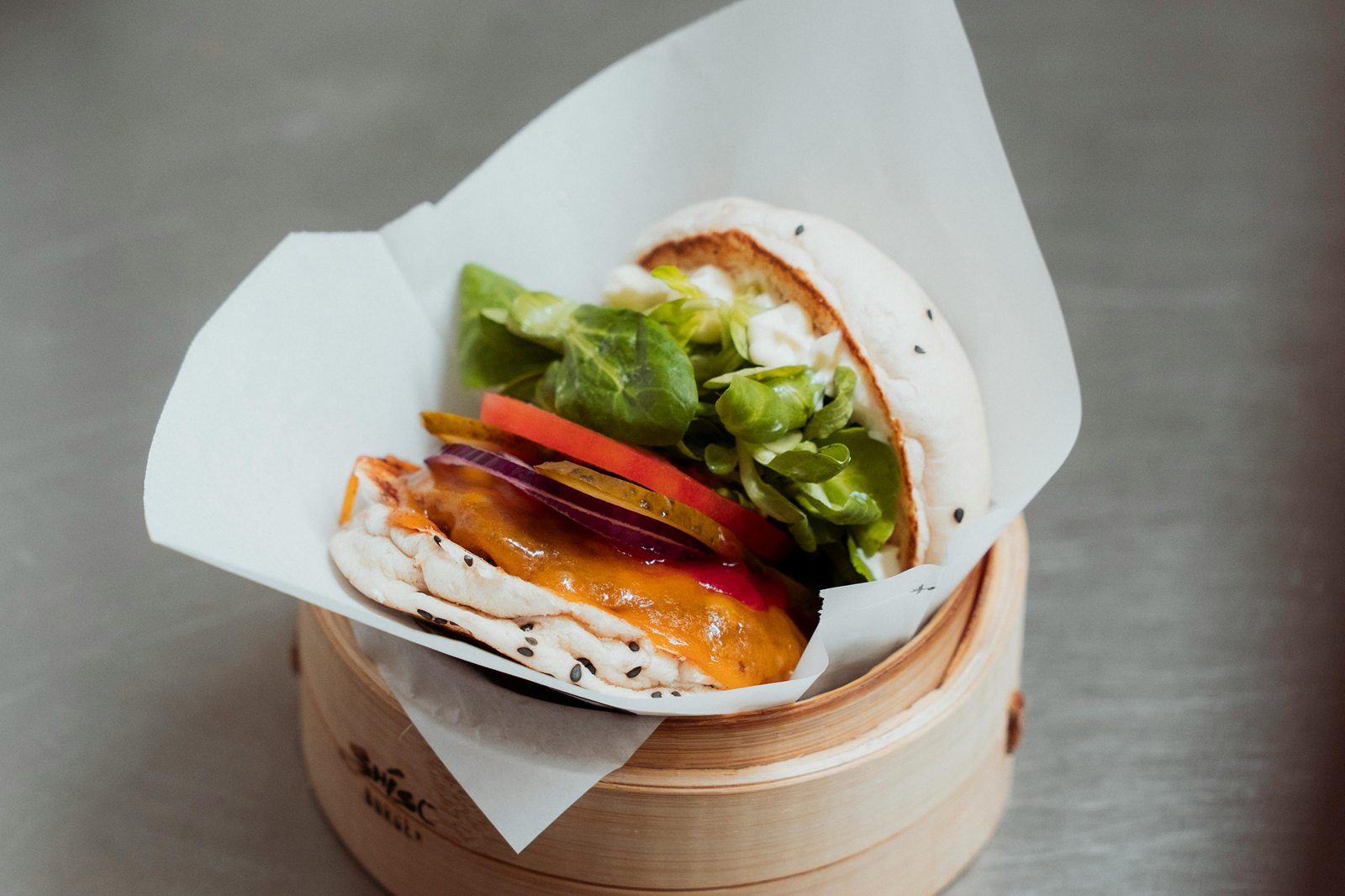 Een burger met kaas, tomaat en sla in wit papier, in een bamboe stoommandje