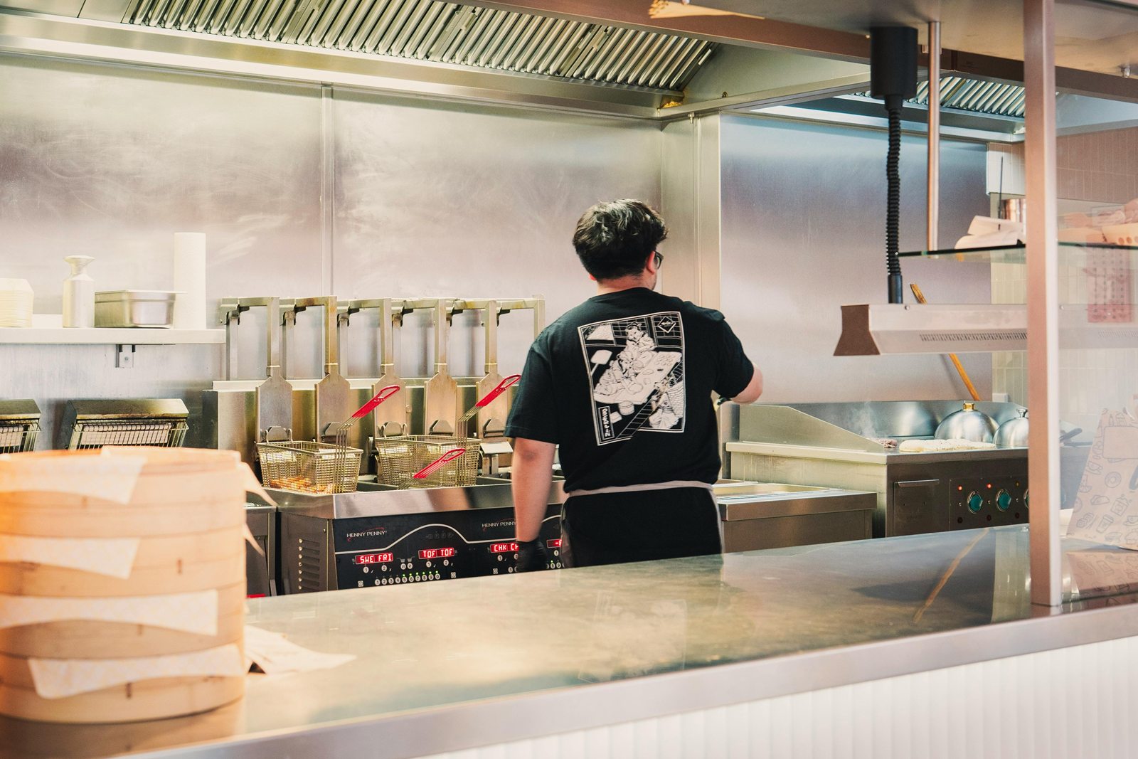 Een medewerker in een zwart Shiso-shirt staat bij de friteuses in de open keuken